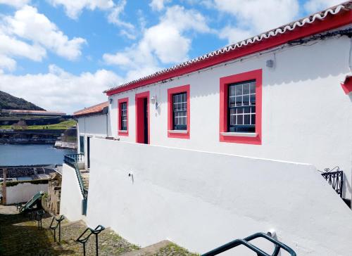 a white building with red windows and a body of water at Casa do Beco in Angra do Heroísmo