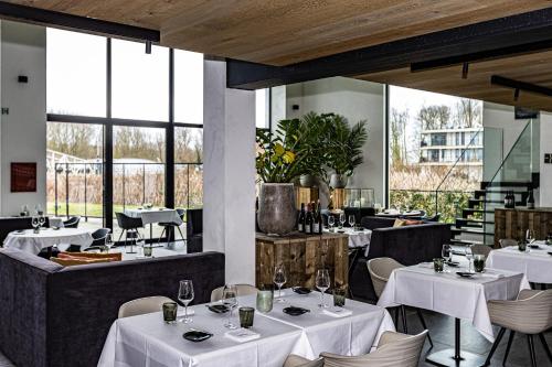 a restaurant with white tables and chairs and windows at De Koolputten in Waasmunster