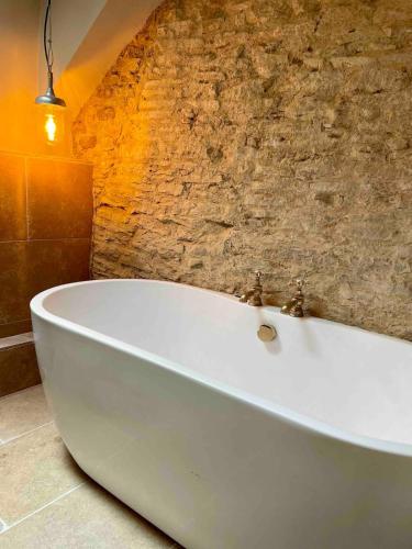 a white bath tub in a bathroom with a stone wall at Highend Cotswold Barn near Soho Farmhouse & Daylesford in Duns Tew