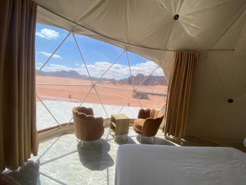 a bedroom with a bed and chairs and a large window at Wadi Rum Santa Camp in Wadi Rum