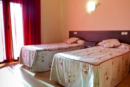 two beds in a room with red curtains at Hotel Casa Marzo in Cariñena