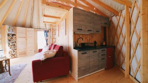 a living room with a red couch and a kitchen at Glamping Niebiańska Osada Jurty Dolnośląskie & SPA in Polanica-Zdrój