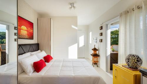 Un dormitorio con una gran cama blanca con almohadas rojas. en Studio com churrasq 650m da Torre Panorâmica RME047, en Curitiba