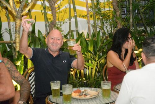 a man sitting at a table holding up glasses of beer at Happy Bear Hostel Phu Quoc in Phu Quoc