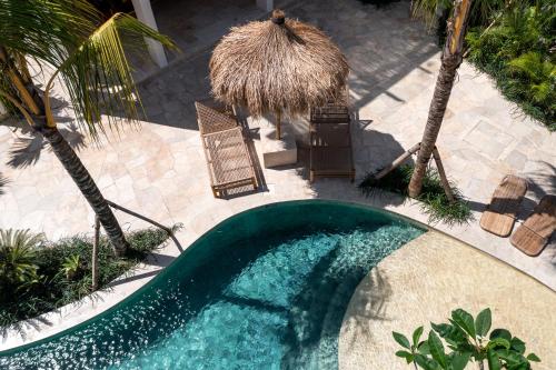 an empty swimming pool with a straw umbrella and palm trees at Mayiki Boutique Hotel in Uluwatu
