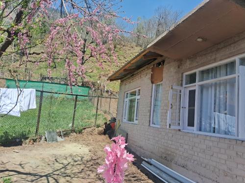 a house with a fence and a tree with pink flowers at Mountain side homestay in Pahalgām