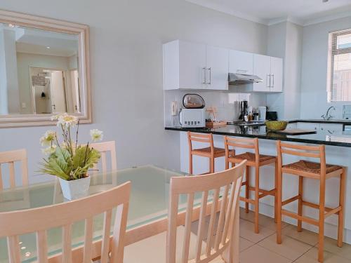 cocina con mesa de cristal y algunas sillas en The Waves Empire Apartment, en Muizenberg