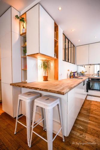 une cuisine avec des placards blancs et un comptoir en bois avec des tabourets dans l'établissement Appartement Design - Lumineux & Confort - 5mn de Paris, à Bagnolet
