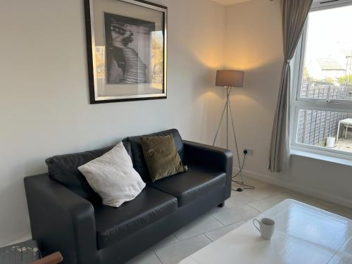 a living room with a black leather couch and a window at Large triple room in Canada Water London in London