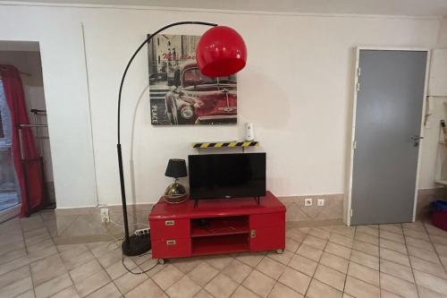 un salon avec une télévision et une table rouge avec une lampe dans l'établissement Le Moulin - Grand studio - Gare, à Narbonne
