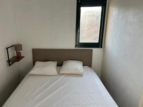 un letto con due cuscini in una stanza con finestra di Appart Gwen a Gruissan