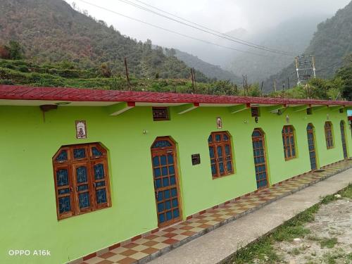 a green building with wooden windows with mountains in the background at Green Hills Homestay in Dhanaulti