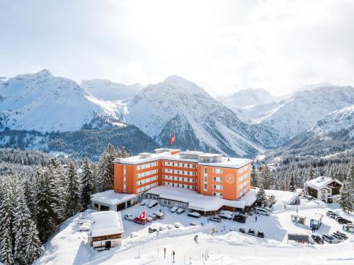 a hotel in the snow with mountains in the background at Hotel Prätschli in Arosa