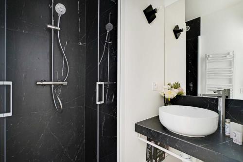 La salle de bains en noir et blanc est pourvue d'un lavabo et d'une douche. dans l'établissement Chic apartment - 2BR 6P - Saint-Ambroise, à Paris