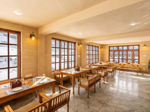a restaurant with wooden tables and chairs and windows at Moustache Koksar Luxuria, Sissu in Khoksar