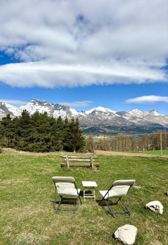 two chairs and a bench in a field with mountains at Chalet Joue du loup 6-7 pers in Le Dévoluy