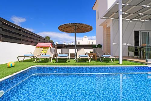 a swimming pool with chairs and an umbrella next to a house at Villa White Star - 100m from Serena Beach in Protaras