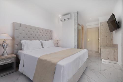 a white bedroom with a large bed and a television at Mythos Panorama - Adults Only in Boukari