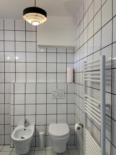 a white tiled bathroom with a toilet and a sink at LightHouse in Albissola Marina