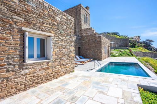 an external view of a stone house with a swimming pool at Olea Tinos, A Luxury Villa in Kardiani