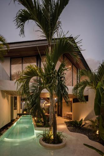 a palm tree in front of a house with a swimming pool at Can Maestro Bali by House of Winds - Lush Sanctuary near Canggu in Kerobokan