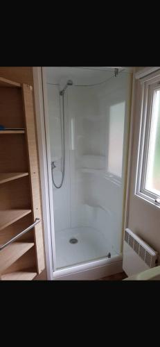 La salle de bains est pourvue d'une douche blanche et d'une fenêtre. dans l'établissement Cabane du bonheur, à Saint-Chéron