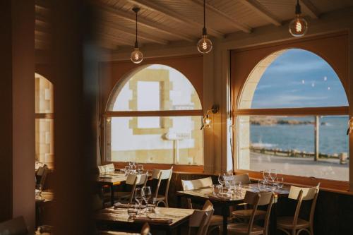 a restaurant with tables and chairs and two windows at Rivage, Chambres et Table in Saint-Pierre-Quiberon
