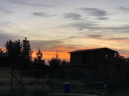 a house in a field with a sunset in the background at Tiny House Casa Maqui in Cáhuil