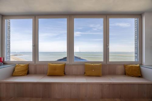 a bench in a room with four windows with yellow pillows at Hello Zeeland - Appartement Port Scaldis 01-081 in Breskens