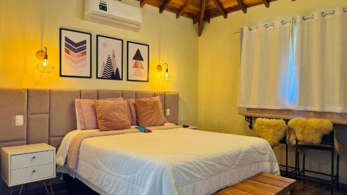 a bedroom with a bed with white sheets and yellow walls at Chalés Vila do Moinho in Monte Verde