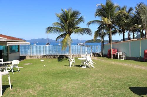 a yard with white chairs and palm trees and the water at Pousada do Contorno in Angra dos Reis