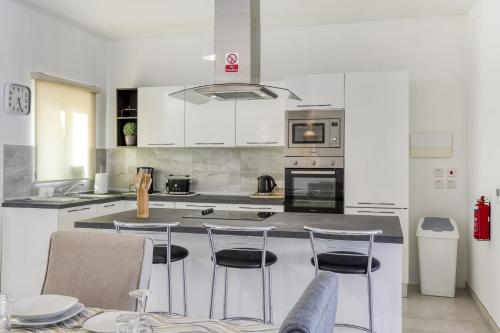 a kitchen with white cabinets and a island with bar stools at Fleur de Mai penthouse with large terrace in Gzira in Taʼ Xbiex