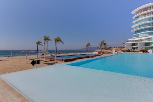 a swimming pool next to a beach with a building at Aria Ocean Condominios in Nuevo Vallarta 