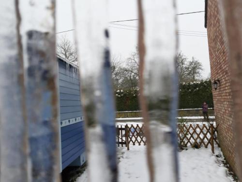 a fence with a blue building in the snow at Charming Caravan Near Hamois with Garden in Chevenia