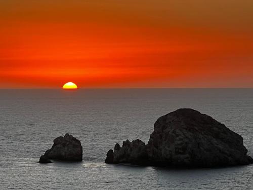 a sunset over the ocean with rocks in the water at Hotel La Siesta Malecón in Mazatlán
