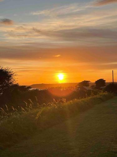 a sunset over a field with the sun in the sky at Ardmore's Modern Beach House in Ardmore