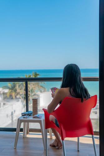 a woman sitting in a red chair looking out at the beach at Condo vista al mar, alberca rooftop Chixchulub in Chicxulub