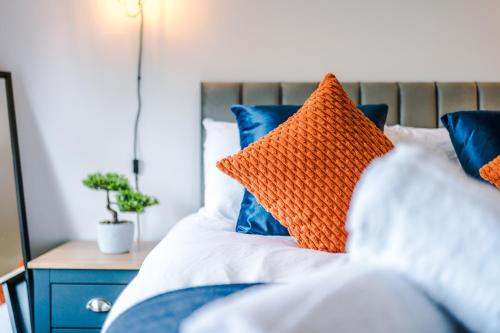 an orange pillow on a bed with blue pillows at NEW! The Acacia House Lodge - Modern & Stylish 3 Bed By Parydise Properties Ltd - Ideal for families or business stays! in Shevington