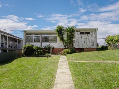 a house with a grass yard in front of it at Boardwalk Bungalow - pristine ocean views in Urunga