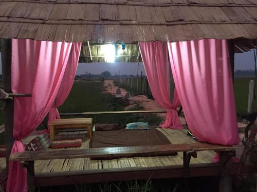 Cama con cortinas rosas en un porche de madera en OrganicHomeFarmStay, en Ban Na Sông