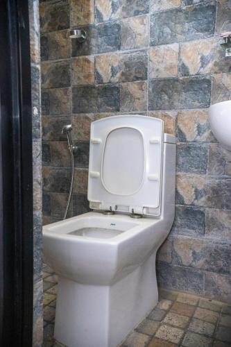 a white toilet in a bathroom with a stone wall at k2Homes in Pātan