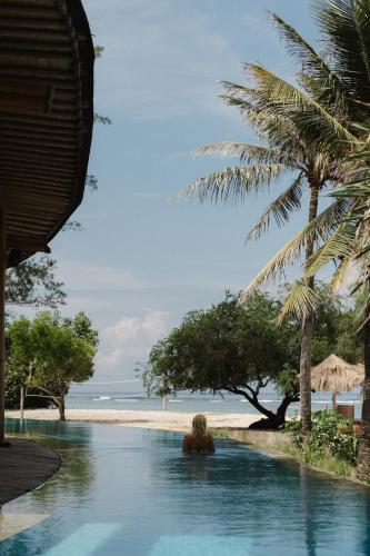 a woman sitting in a swimming pool next to a beach at Hotel Lumi Gili Trawangan in Gili Trawangan
