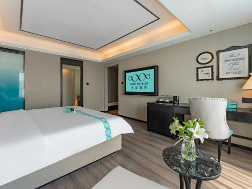 a bedroom with a bed and a table and a tv at XANA Hotel Qionghai Municipal Government High-speed Railway Station in Qionghai