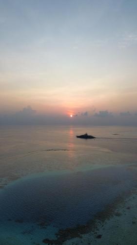 an island in the ocean with the sunset in the background at Rattehi Inn at Rakeedhoo in Rakeedhoo