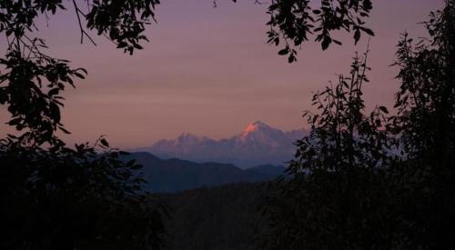 a mountain in the distance with the sun shining on it at Saanjh Binsar, Himalaya ka Dwaar in Hawālbāgh