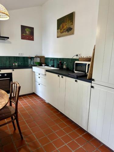 une cuisine avec des armoires blanches, une table et un micro-ondes dans l'établissement Le cottage à 40 min de Paris, à Luzarches