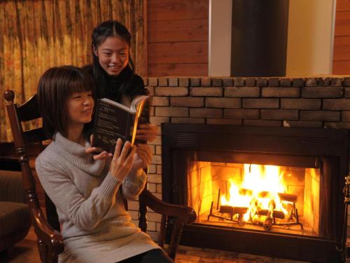 two women reading a book in front of a fireplace at Izumigo AMBIENT Azumino Cottage in Azumino