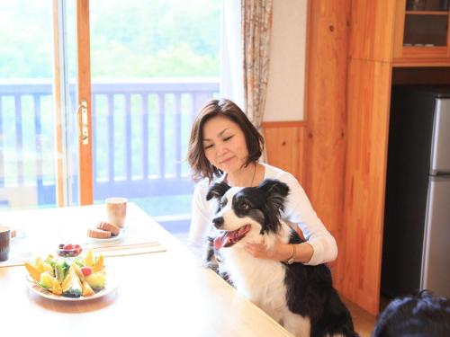 a woman sitting at a table with a dog at Azumino Wanwan Paradise Cottage in Azumino