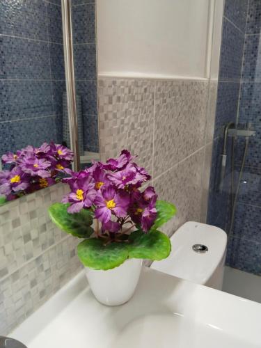 a white vase with purple flowers sitting on a bathroom sink at Los Eucaliptos in Fasnia