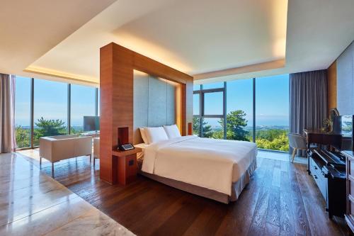 a bedroom with a large bed and large windows at WE Hotel Jeju in Seogwipo